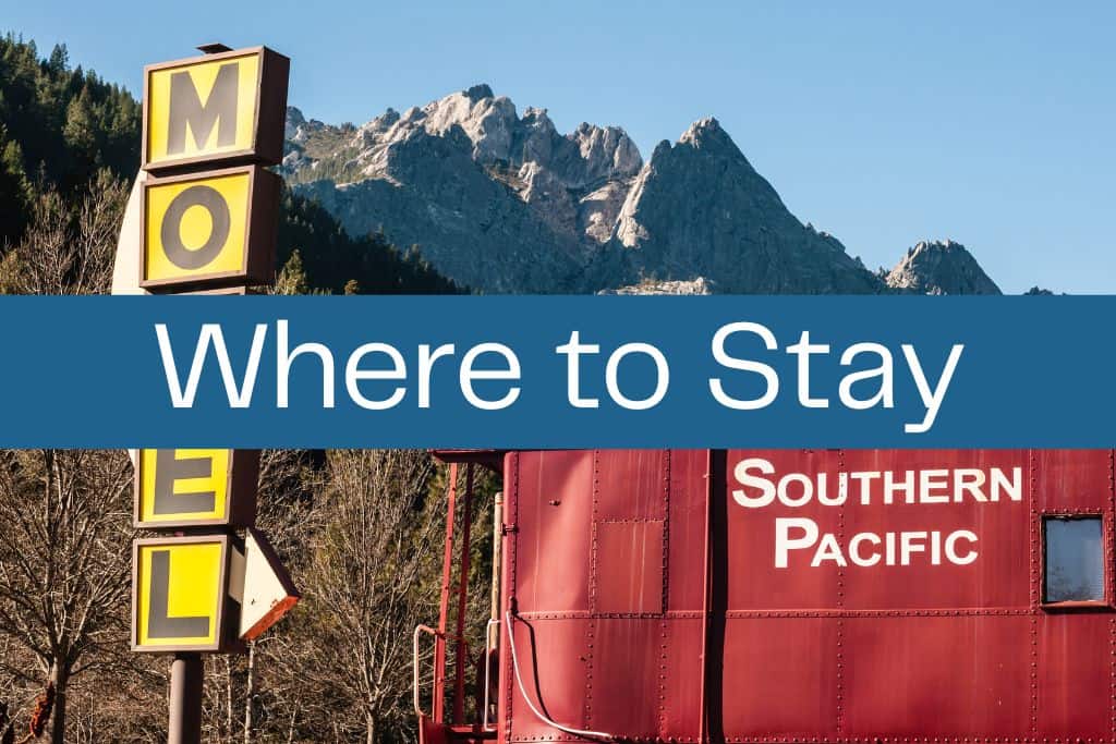 Retro yellow motel sign and a red Southern Pacific train car set against a backdrop of forested hills and jagged mountain peaks. A bold blue banner across the center reads "Where to Stay" in large white text.